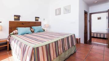 Un dormitorio con cabecera de madera, cubrecama a rayas, dos almohadas, lámparas de noche y una mesita de noche con lámpara.