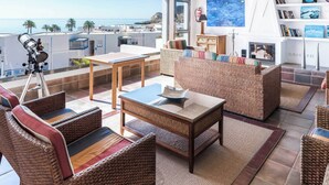 Un salón soleado con muebles de mimbre, un telescopio y vista al mar.