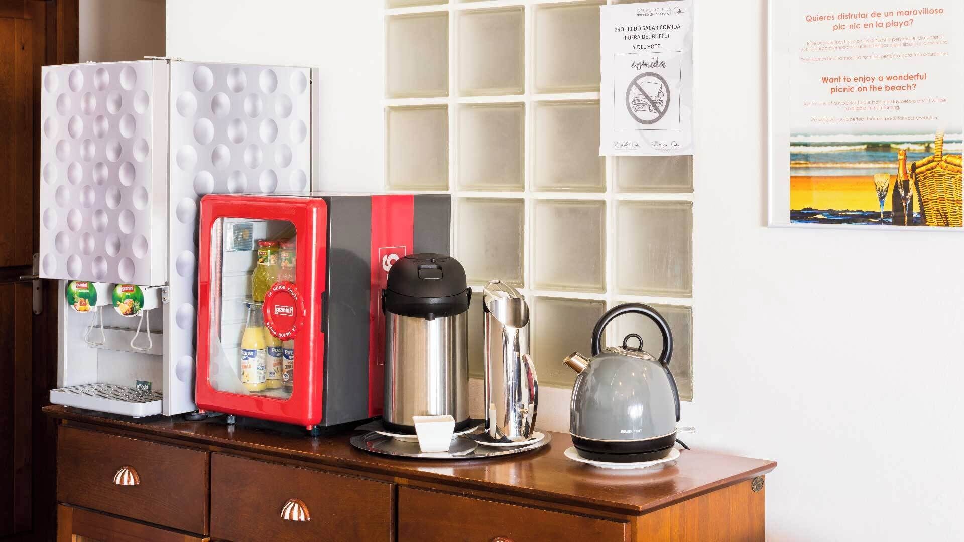 Uma cozinha compacta com geladeira, cafeteira, chaleira e micro-ondas.