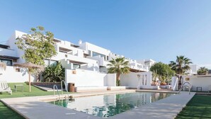 Un edificio moderno con piscina, rodeado de palmeras y un césped bien cuidado.