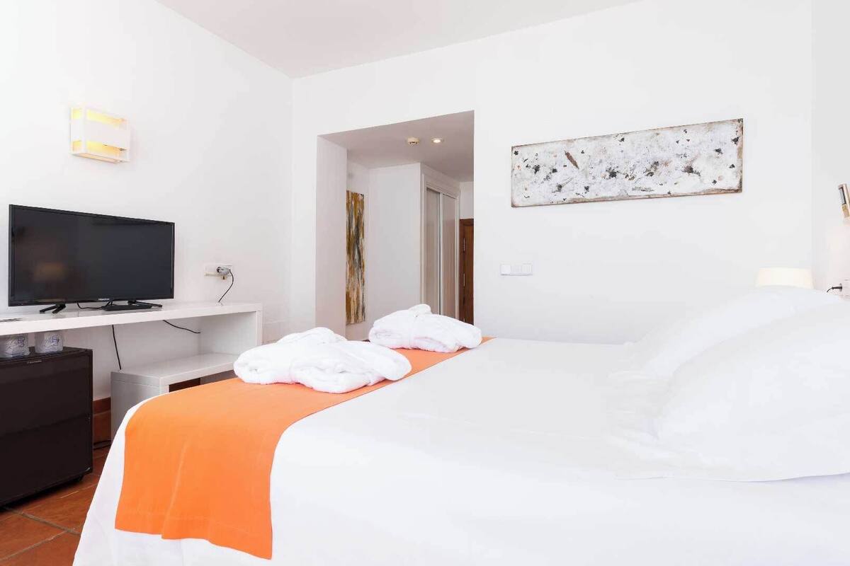 A hotel room with a bed, a TV, a desk, and a painting on the wall.