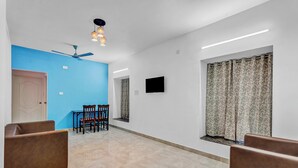 Una habitación amplia con una pared azul de acento, un ventilador de techo, un televisor de pantalla plana y una ventana con cortinas estampadas.