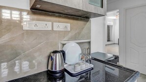 Cocina moderna con salpicadero de mármol, cafetera, hervidor y una bandeja con tazas y azúcar.