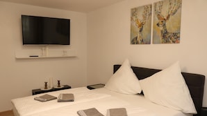 A neatly made bed with white linens and two pillows, a flat-screen TV mounted on the wall, and two paintings of deer on the wall. - Apartment in Essen with Garden Terrace (Essen)