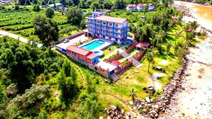 A large hotel with multiple floors, a swimming pool, and a view of a river and mountains. - River Beach Resort - Trishuli (Dhussa)