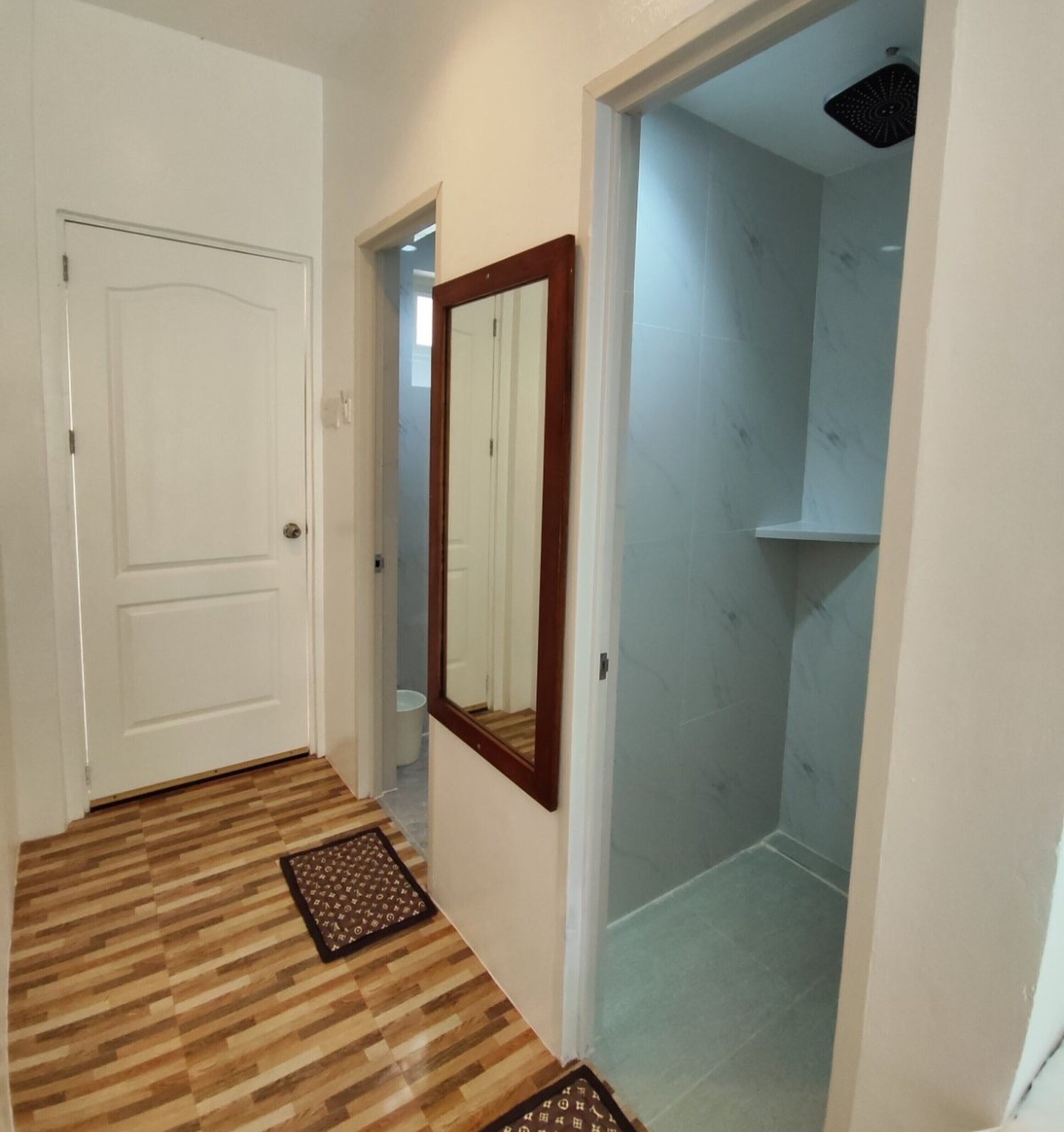 A hallway with a wooden floor, a white door, and a mirror on the wall.