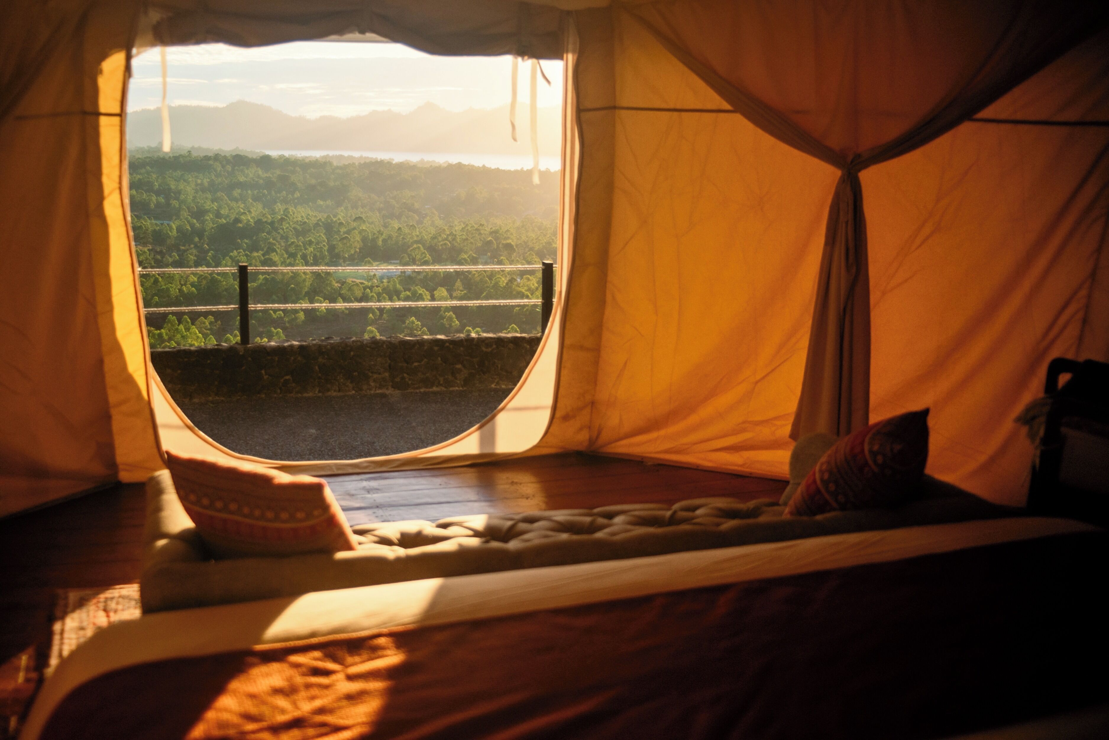 A tent with a bed inside, a view of a forest through a window, and a mountain in the background.