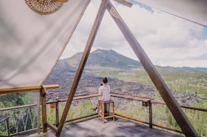 Una persona sentada en un taburete de madera en un balcón con vistas a una montaña.