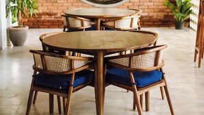 A round wooden table with four wicker chairs, a large round window, and a brick wall. - Alam Caldera Camp & Resto  (Kintamani)