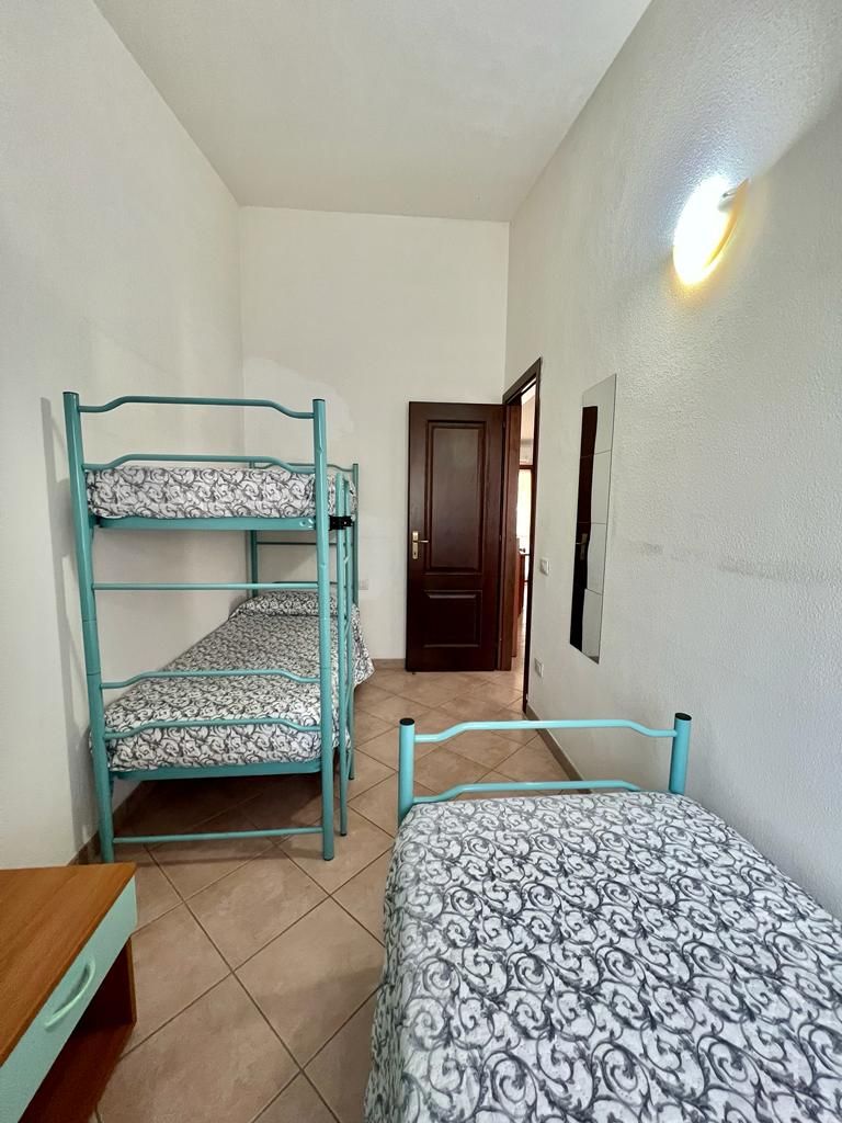 A room with bunk beds, a wooden desk, and a door leading to another room.