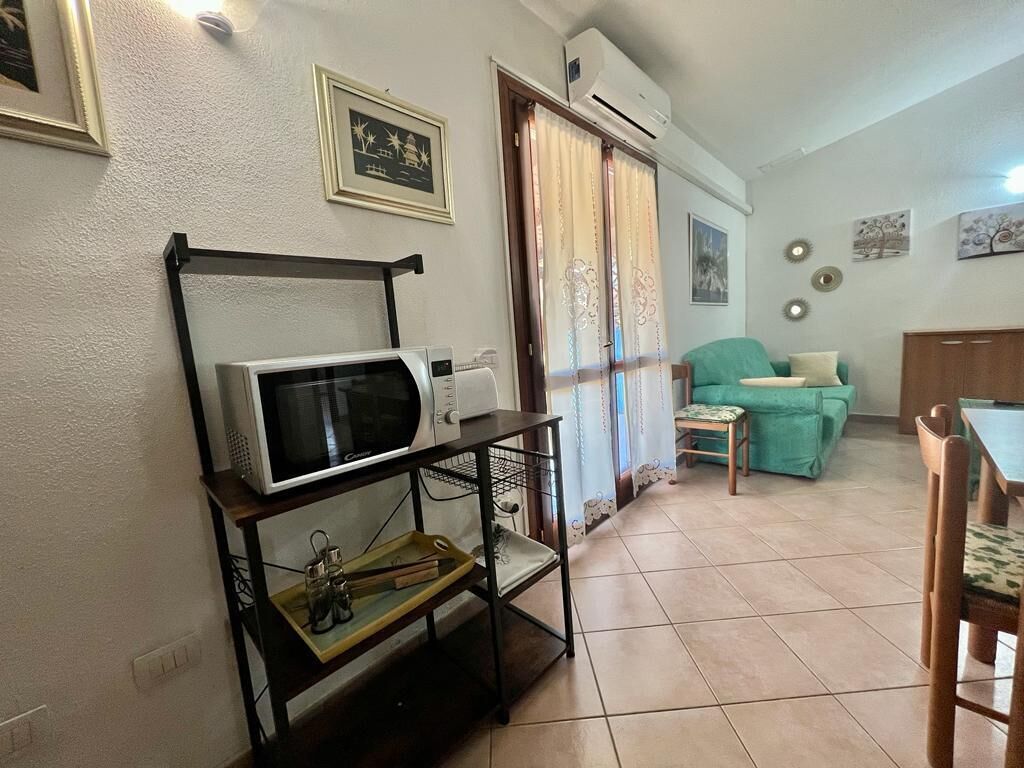 A living room with a microwave on a stand, a teal sofa, and a dining table with chairs.