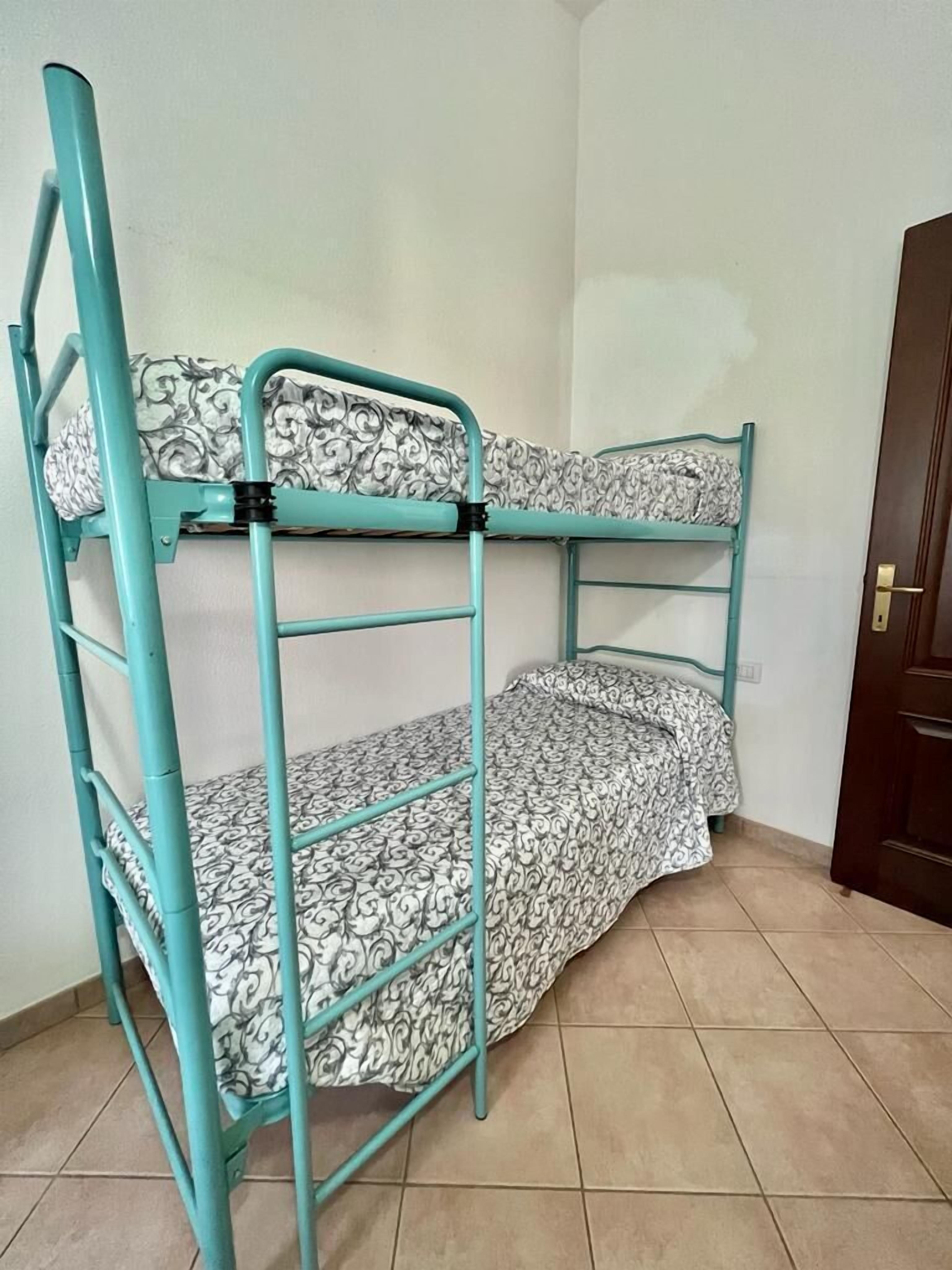 A bunk bed with patterned bedding in a room with tiled flooring and a door.