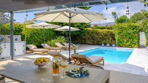 Zona de piscina con sillones, sombrillas y una mesa con un bol de limones y bebidas.