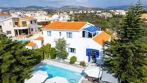 Una villa moderna con piscina, varios balcones y vistas del vecindario circundante.