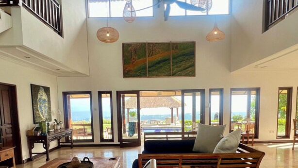 A spacious living area with a high ceiling, large windows, and a view of the outdoors.