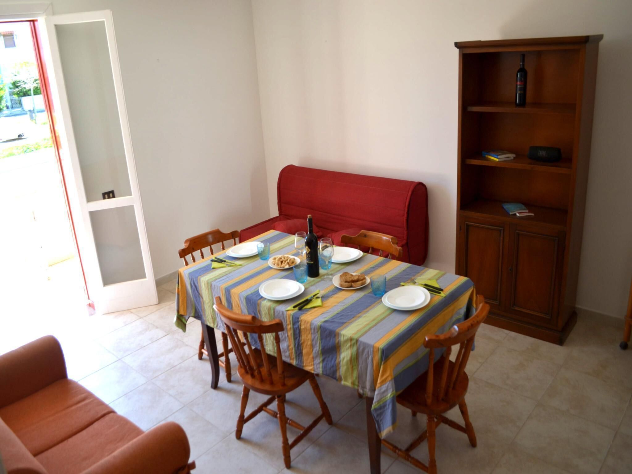 Un'area pranzo con un tavolo apparecchiato per due, una panca rossa e una libreria in legno.