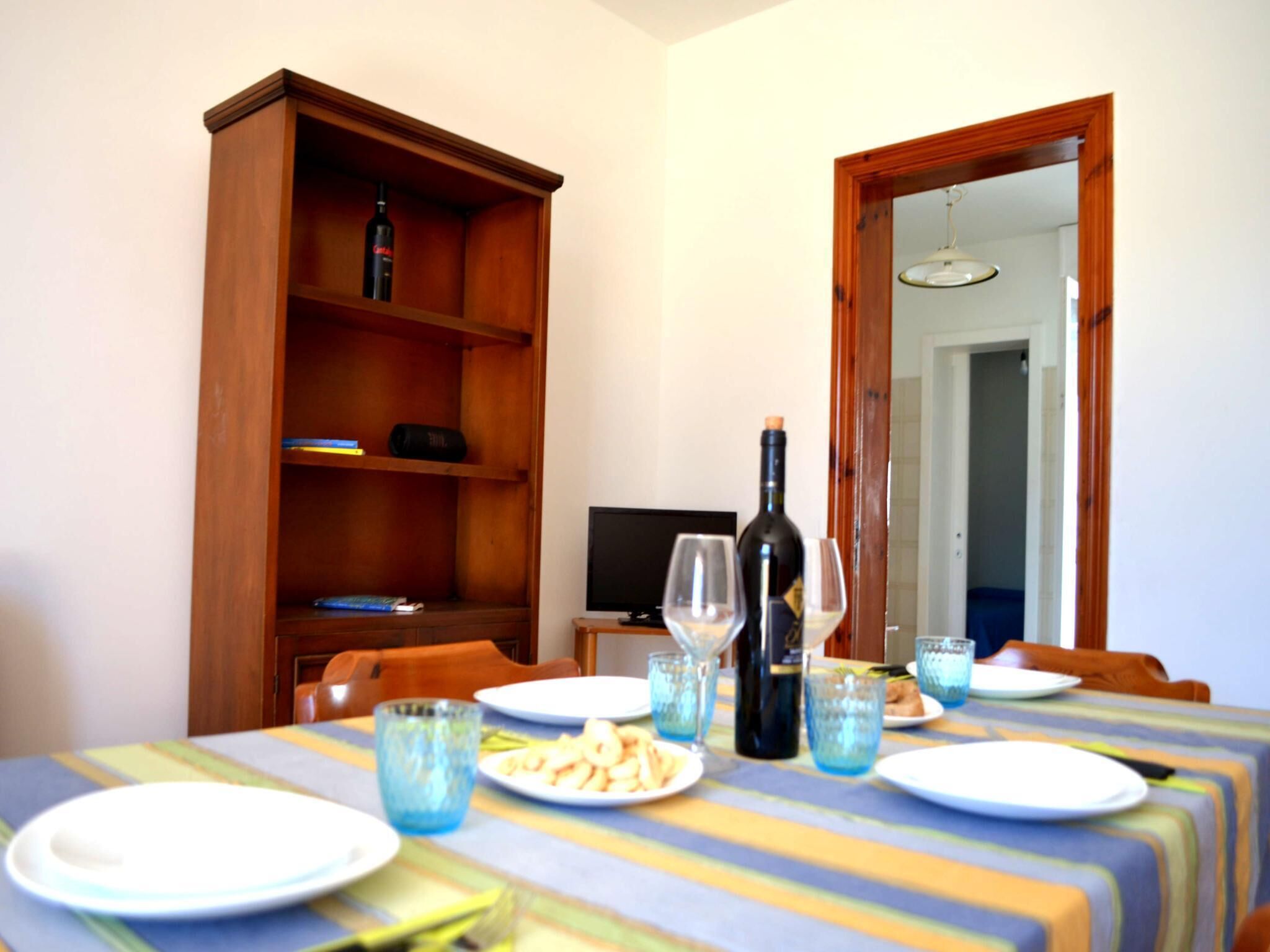 Un coin repas avec une table dressée pour deux personnes, une bibliothèque en bois et un téléviseur en arrière-plan.