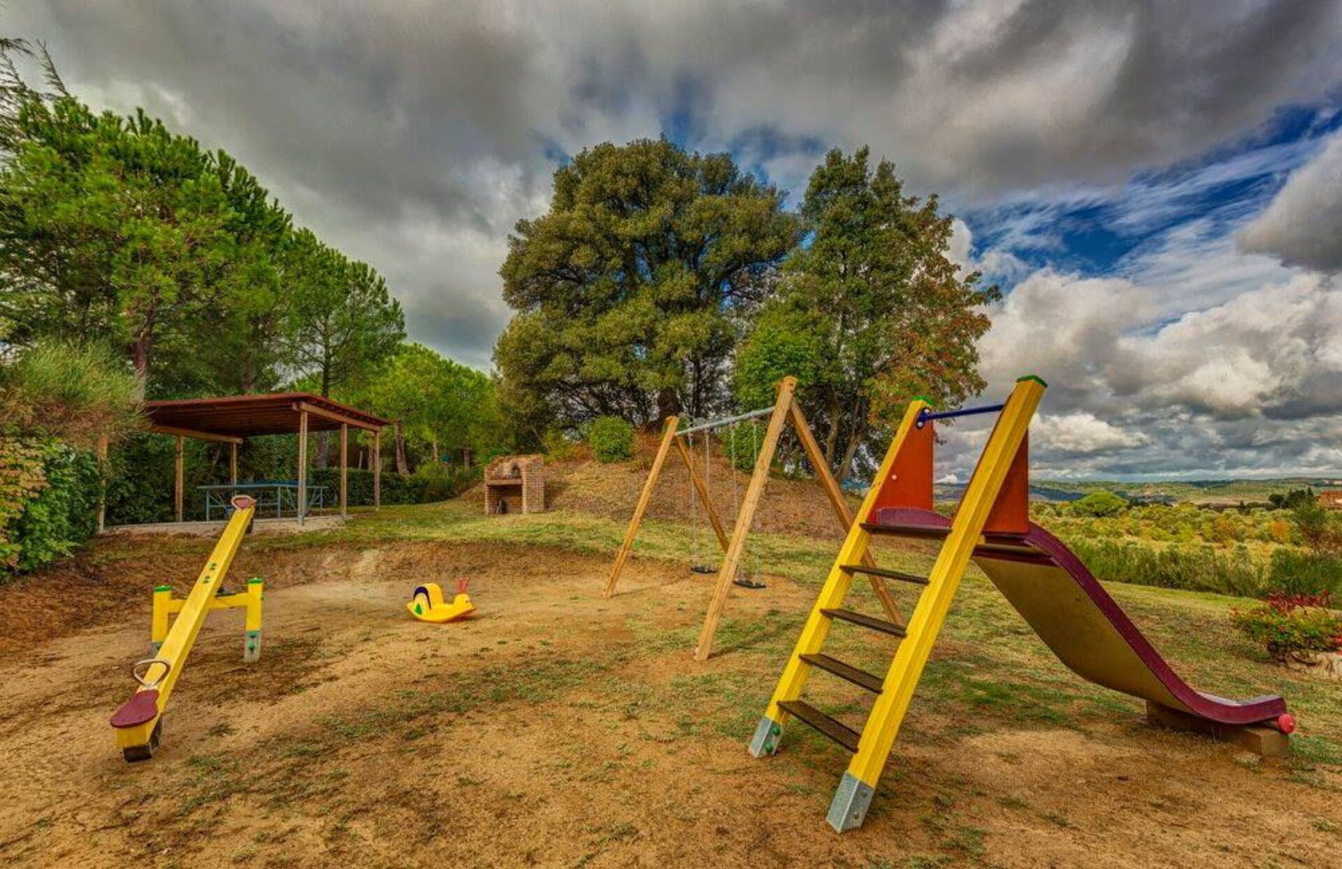 Un parque infantil con columpios, tobogán y zona de estar cubierta.