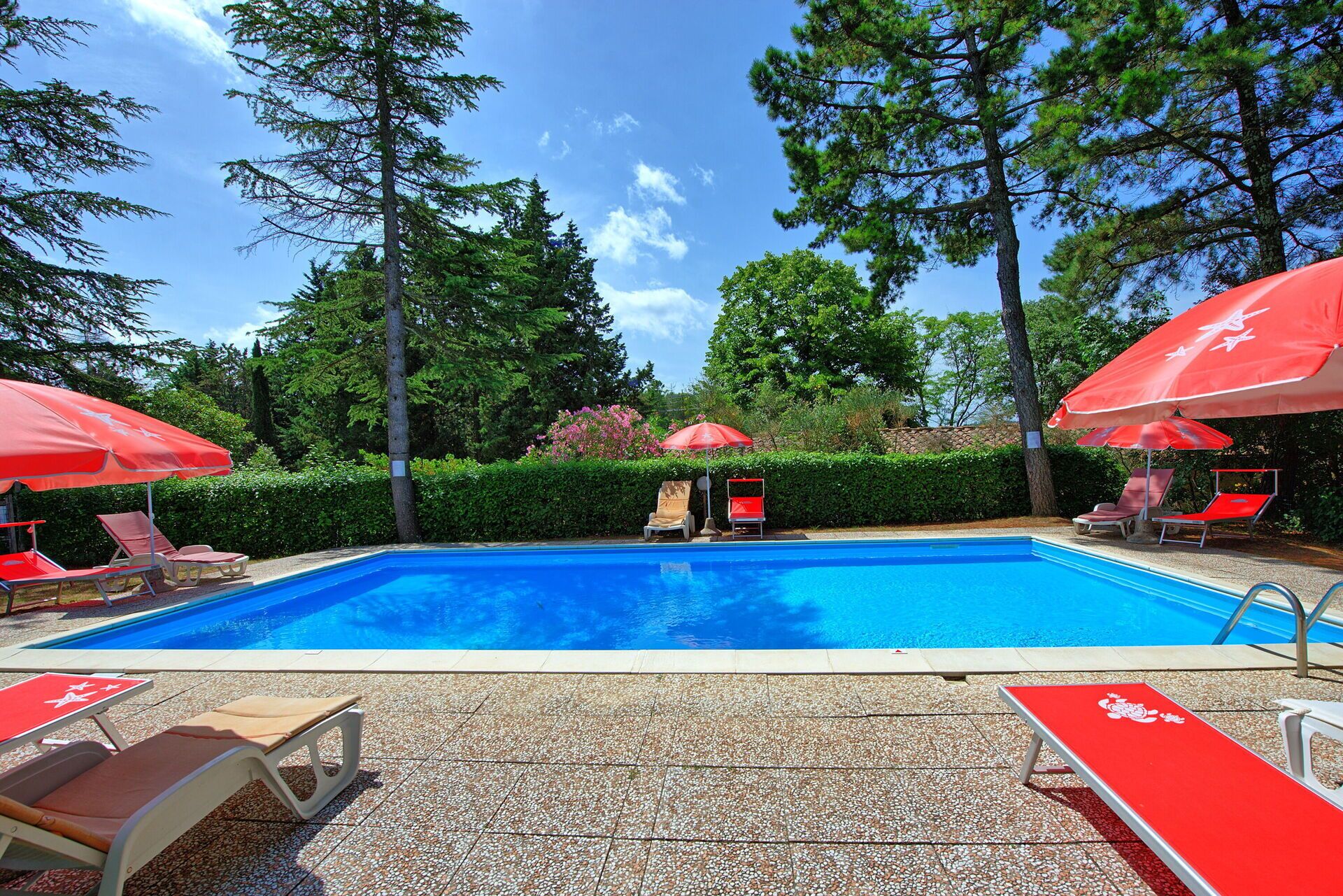 A swimming pool with red umbrellas and lounge chairs.