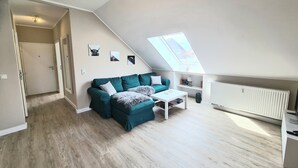 Un salón tipo loft con techo alto, tragaluz, sofá verde, mesa de centro blanca y radiador.