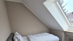 Un dormitorio pequeño y moderno con cama entrepiso, mesita de noche con lámpara y tragaluz.