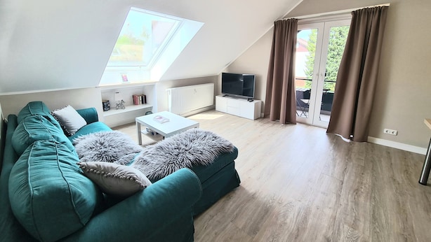 Una sala de estar moderna con un sofá color turquesa, una mesa de centro blanca y un televisor sobre un mueble blanco. Hay un tragaluz y un ventanal corredizo al exterior.