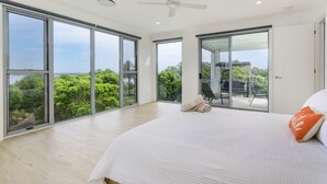 Un dormitorio amplio con puertas de cristal correderas que dan a un balcón, una cama con edredón blanco y vistas a la vegetación.