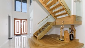 Un interior moderno con una escalera de madera, barandillas de vidrio y una plataforma de madera decorada.