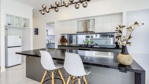Una cocina moderna con una isla central, taburetes blancos y una planta decorativa.