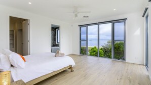 Un dormitorio con una cama grande, un ventilador de techo y vistas al mar a través de ventanales del suelo al techo.
