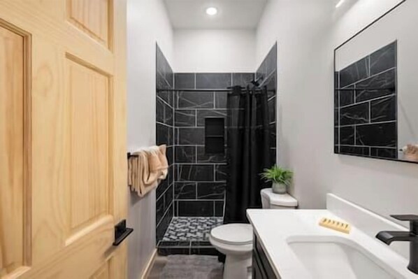 Une salle de bain moderne avec une porte en bois, un lavabo blanc, une douche noire et un sol carrelé.
