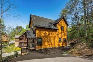 Une cabane en rondins à deux étages, dotée d’un toit à forte pente et entourée d’arbres.