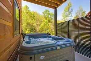 Un bain à remous dans un chalet en bois situé à l’extérieur, avec vue sur les arbres.