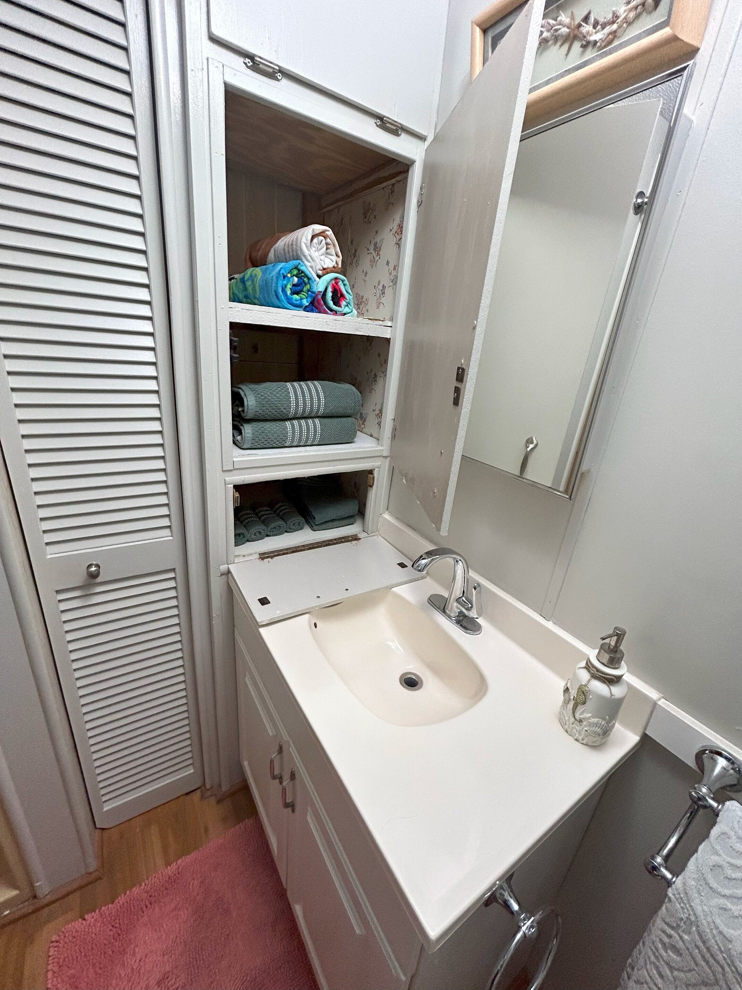 Een badkamer met een wastafel, spiegel en opbergplanken.