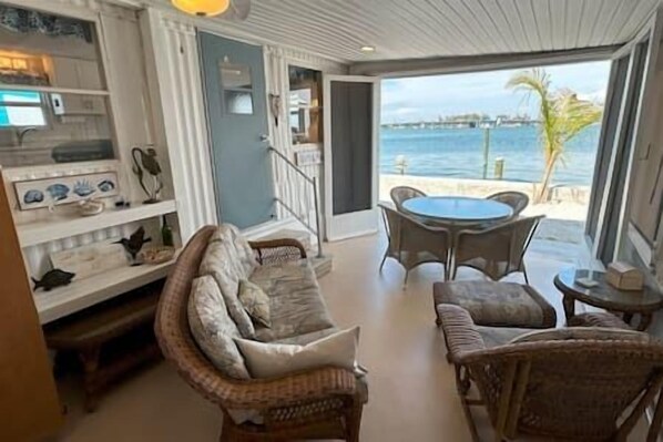 A room with a wicker sofa, a dining table, and a view of the sea.