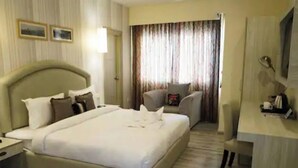 A hotel room with a large bed, a desk, a chair, and a window with curtains. - Hotel Mayvillas Luxury Boutique Stay (Dehradun)
