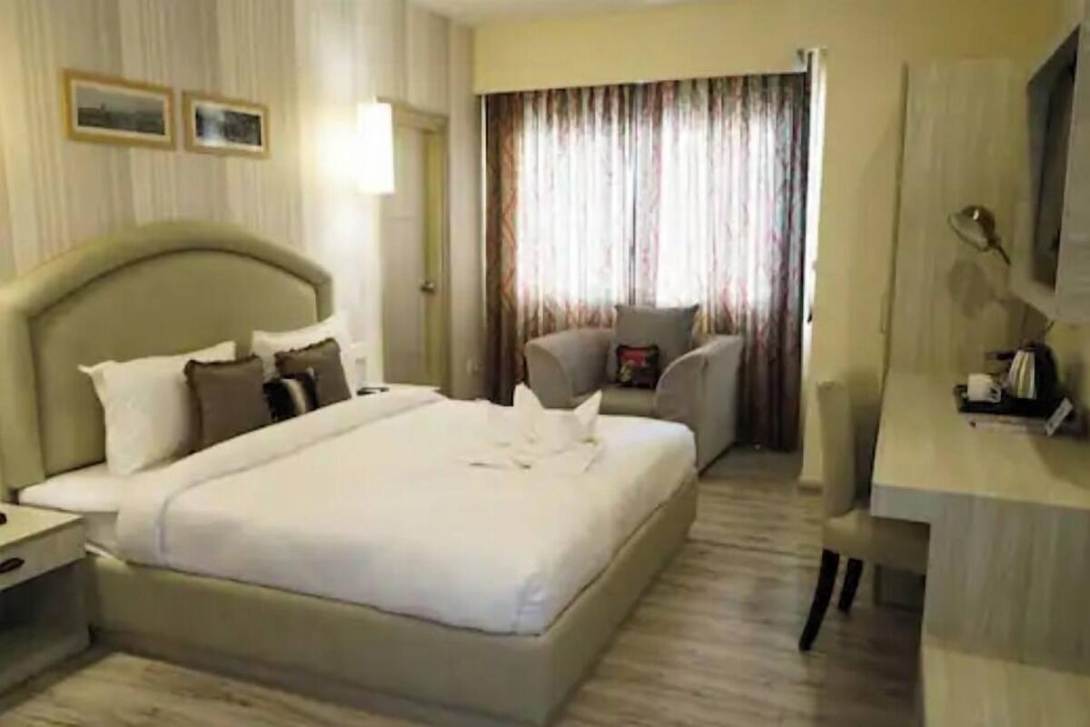 A hotel room with a large bed, a desk, a chair, and a window with curtains.