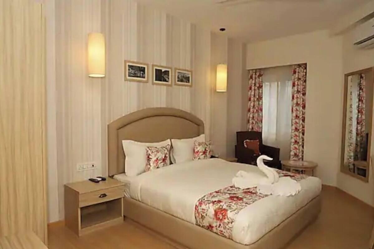 A hotel room with a large bed, bedside tables, a mirror, and wall-mounted lights.