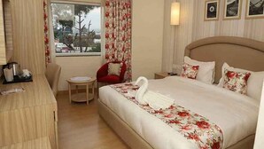 A hotel room with a bed, a desk, a chair, and a window with curtains. - Hotel Mayvillas Luxury Boutique Stay (Dehradun)