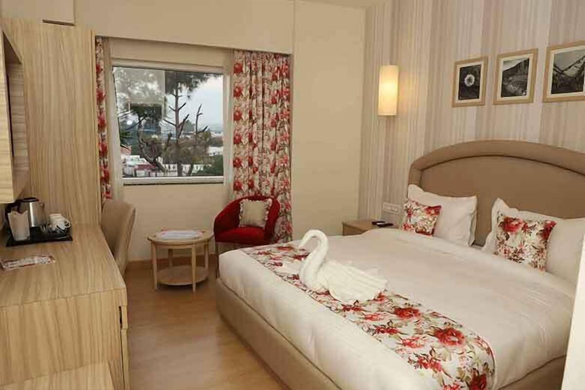 A hotel room with a bed, a desk, a chair, and a window with curtains.