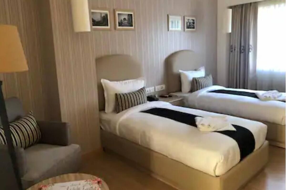 A hotel room with two beds, a sofa, a lamp, and a window with curtains.