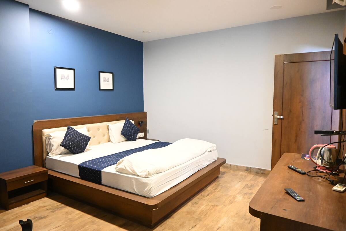 Een slaapkamer met een bed, nachtkastje, houten bureau en een televisie.