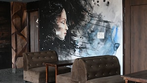 A room with two brown upholstered chairs, a wooden table, and a large abstract painting on the wall. - Hotel Keptown Lite (Jaipur)