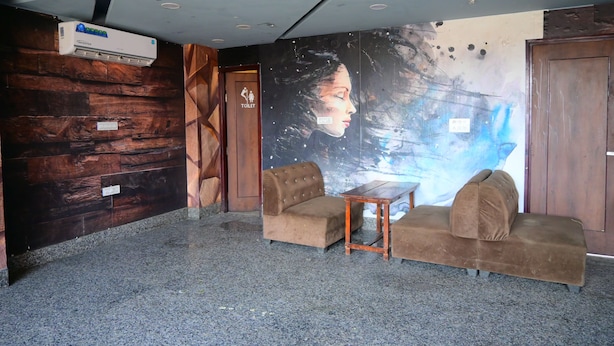 A lobby with a wooden wall, a mural, two sofas, a table, and an air conditioning unit. - Hotel Keptown Lite (Jaipur)