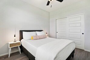 Un dormitorio ordenado con cama, mesita de noche, lámpara y una puerta cerrada.