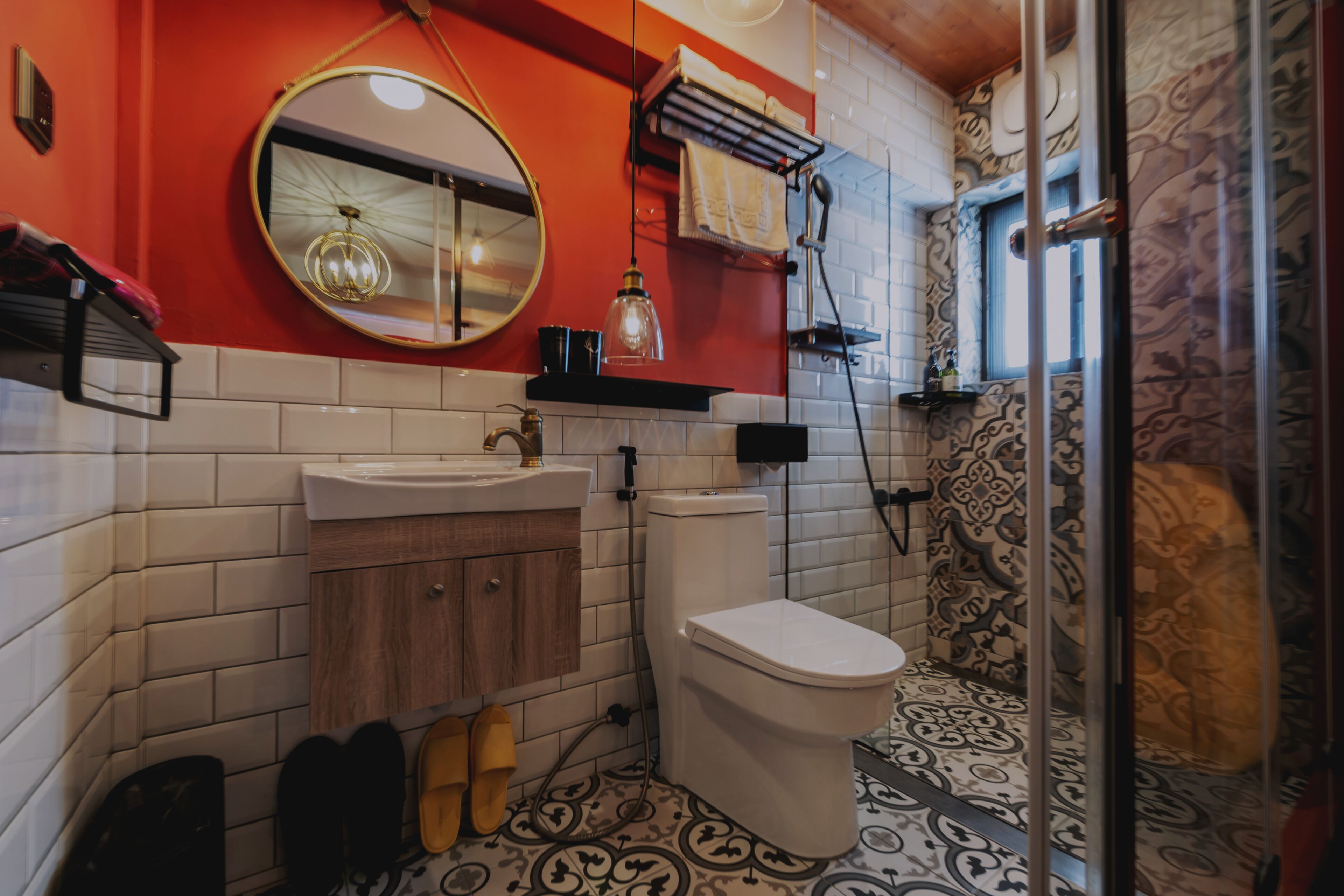 A bathroom with a white toilet, a wooden vanity, a round mirror, and patterned floor tiles.