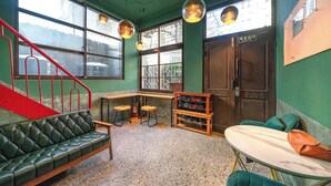 Une pièce avec un mur vert, un canapé en cuir, une table en bois sur laquelle est posée une planche de surf, et un escalier rouge.