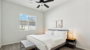 Une chambre à coucher moderne avec un lit, un banc, une table de chevet et un ventilateur de plafond.