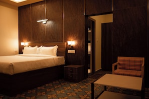 A hotel room with a bed, bedside lamps, a small table, a chair, and a patterned carpet. - Poojaris Niranthara Kabini (Mysore)