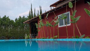 A swimming pool with a red building in the background. - Poojaris Niranthara Kabini (Mysore)